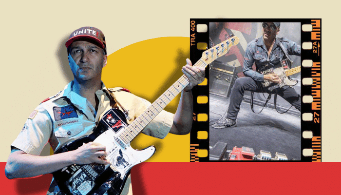 Tom Morello performing live on stage with his pedalboard visible at his feet.