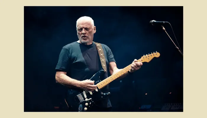 David Gilmour from Pink Floyd performing live with black Fender Stratocaster guitar, wearing black shirt against dark stage backdrop