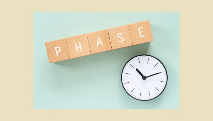 Wooden blocks spelling “PHASE” placed beside a white clock on a light blue background.
